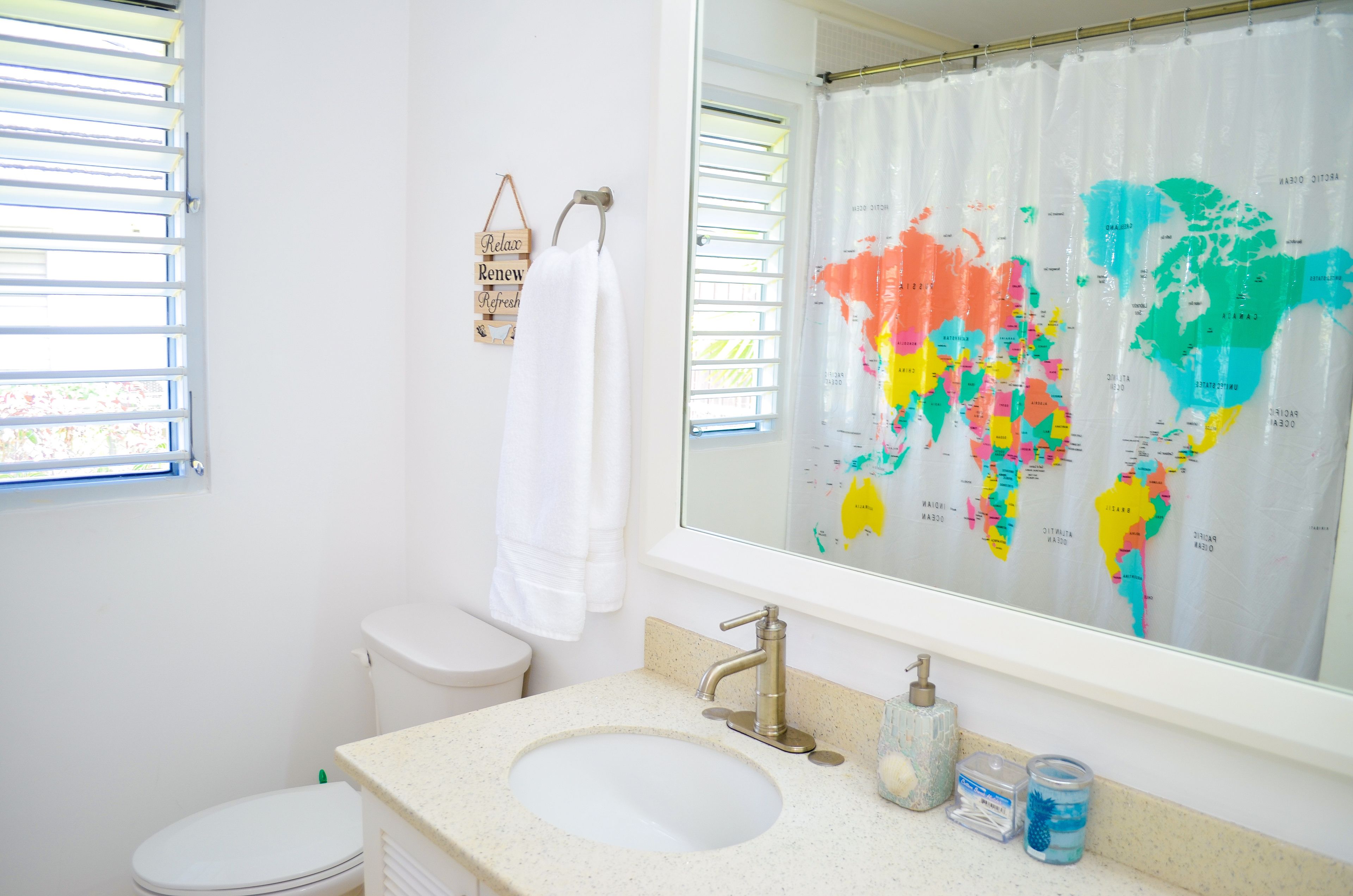 A bathroom with a white toilet, a sink with a faucet, a mirror with a world map, and a towel hanging on the wall.