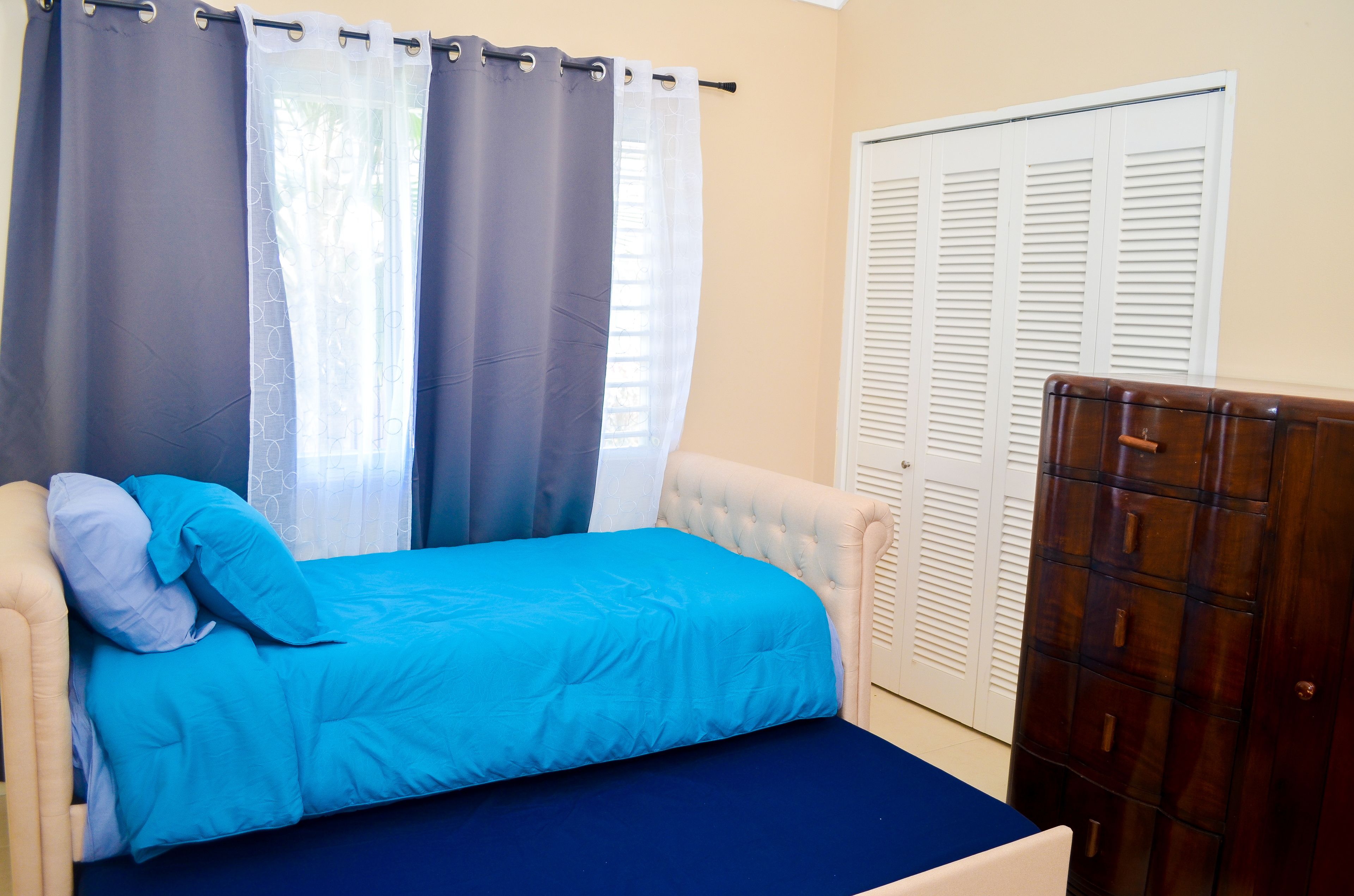 A bedroom with a bed, curtains, a wardrobe, and a window.