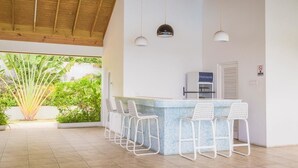 A spacious outdoor area with a bar and seating, featuring a tiled floor and wooden ceiling beams. - Tranquillity at The Palms (St. Ann's Bay)