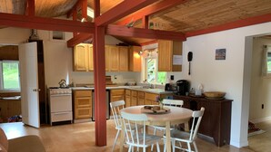 Una cocina acogedora con armarios de madera, una estufa blanca y una zona de comedor con una mesa redonda y sillas blancas.