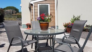 An outdoor patio with a round table and four chairs, surrounded by potted plants and a house in the background. - Comfortable Home in a beautiful part of Dingle Town (Dingle)