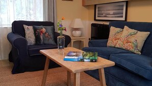 A living room with a dark blue sofa, a wooden coffee table with a book titled "Heritage of Ireland," and a cabinet with glass doors. - Comfortable Home in a beautiful part of Dingle Town (Dingle)