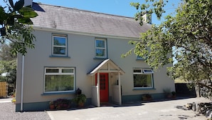 A two-story house with a red door, multiple windows, and potted plants. - Comfortable Home in a beautiful part of Dingle Town (Dingle)