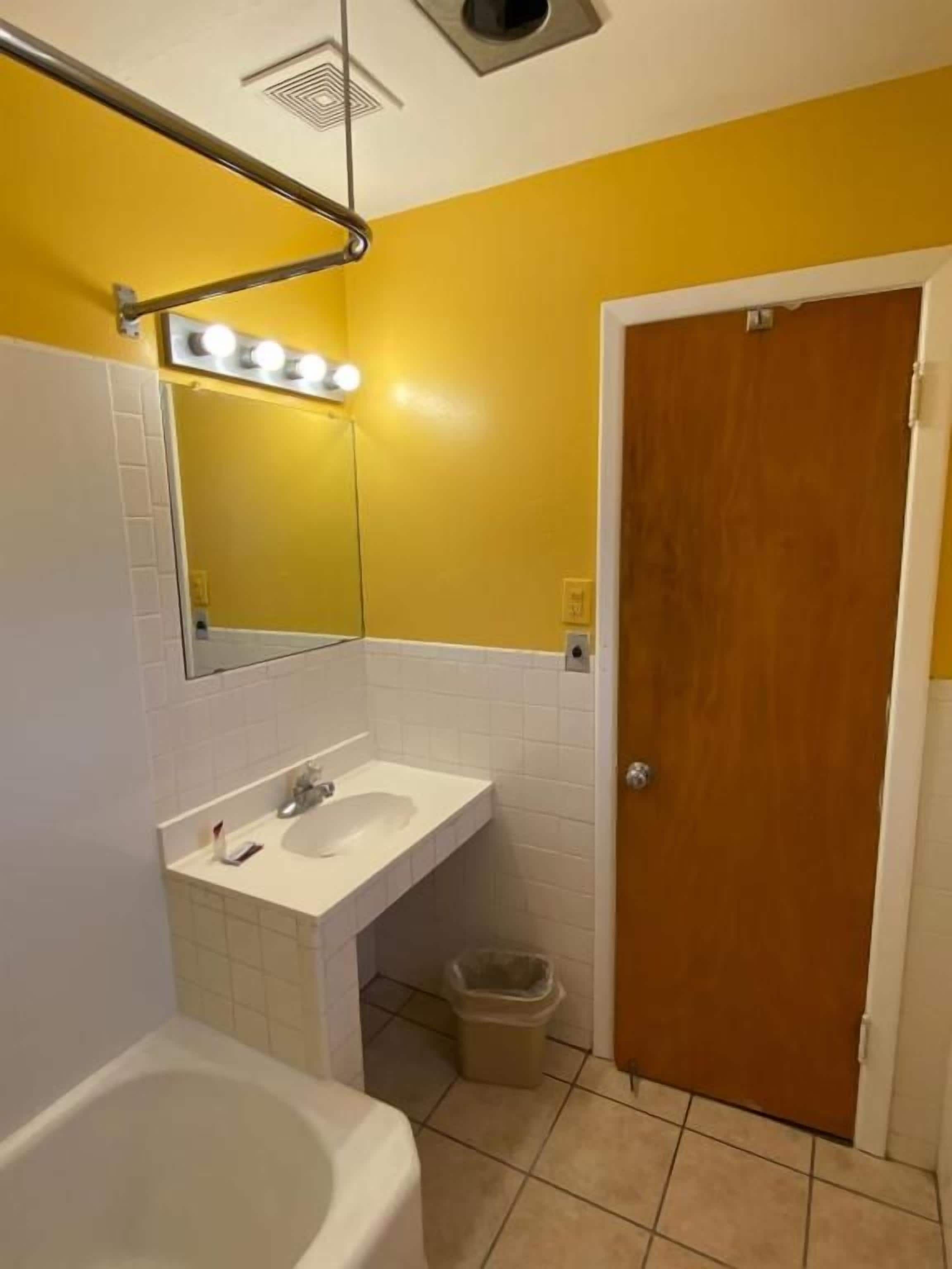 Un baño con un lavamanos blanco, un espejo y una puerta de madera.