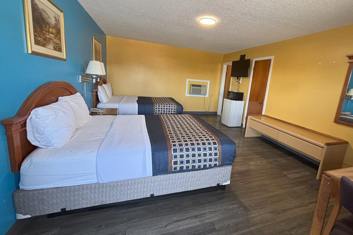 A hotel room with two beds, a desk, a chair, a TV, and a small refrigerator.