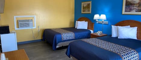 Una camera d'albergo con due letti, una scrivania, una lampada e un quadro appeso al muro.