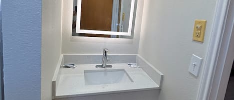Ett litet badrum med ett vitt handfat, en spegel och en papperskorg.