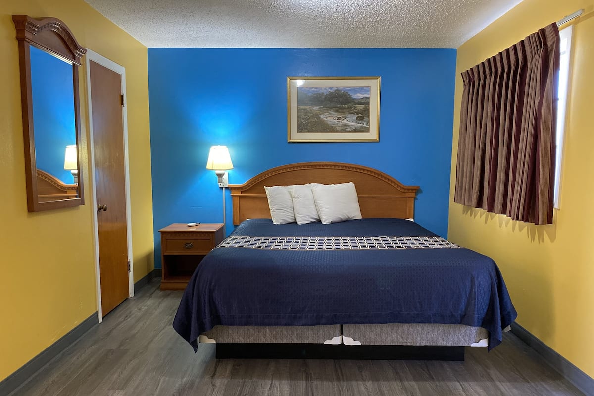 A hotel room with a bed, a nightstand, a lamp, and a picture on the wall.