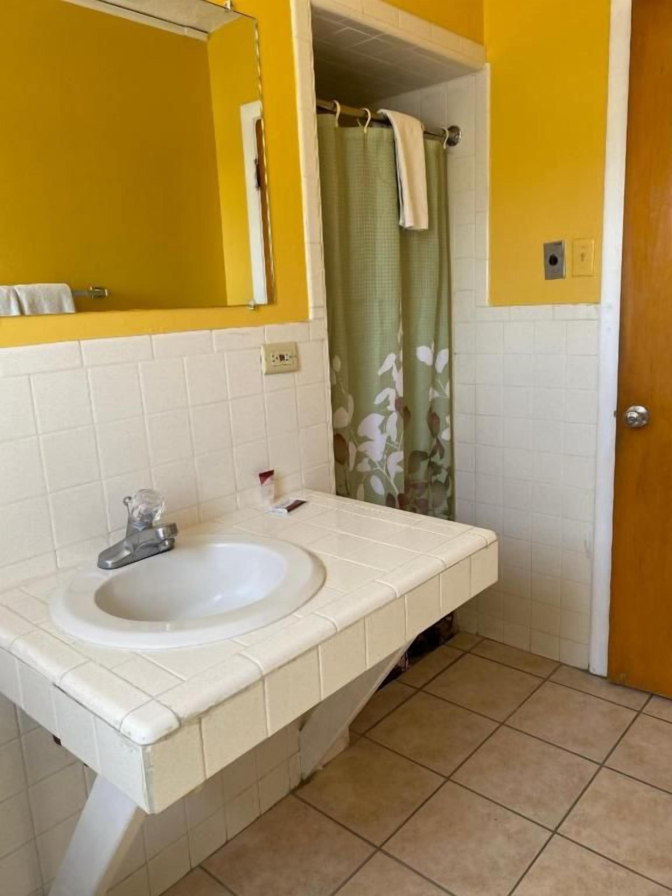 Un baño con lavamanos blanco, espejo y cortina de ducha con estampado floral.