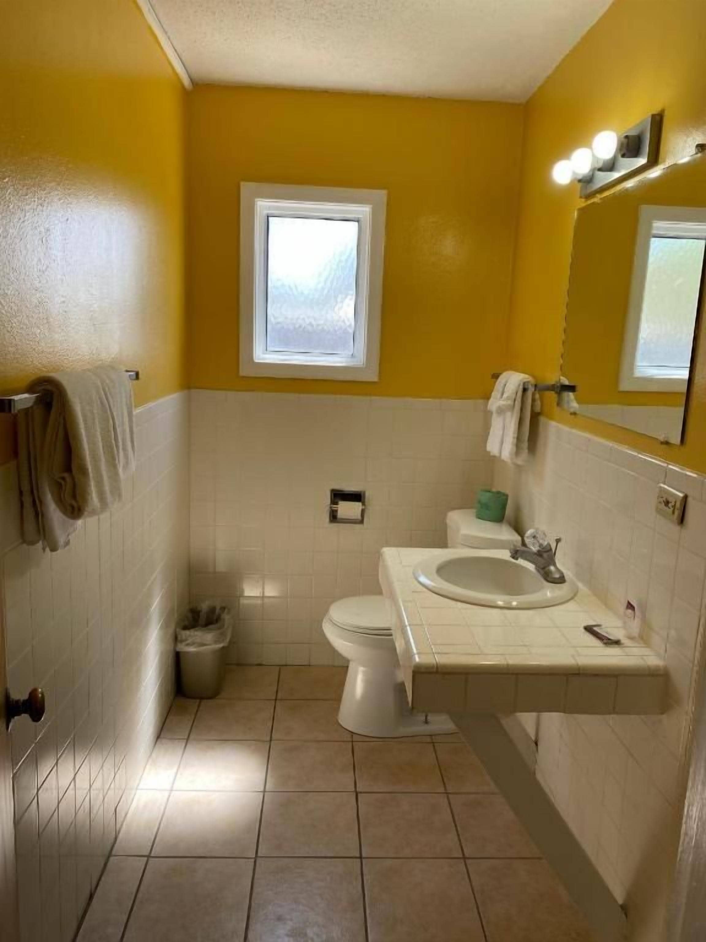 Een badkamer met toilet, wastafel en een raam boven het toilet.
