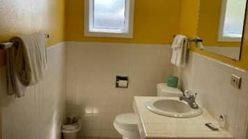Een badkamer met toilet, wastafel en een raam boven het toilet.
