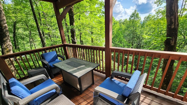 A wooden deck with wicker furniture and a table, surrounded by lush greenery. - Relaxing big sky views early booking discounts for Summer! (Highlands)