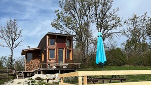 Una cabaña rústica con una terraza de madera, una mesa de picnic cubierta y una pila de leña.
