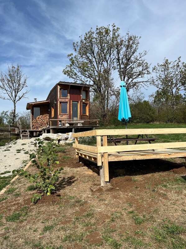 Una cabaña rústica con una terraza de madera, una mesa de picnic cubierta y una pila de leña.