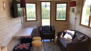 Un acogedor interior de cabaña con paredes de madera, un sofá, un sillón, una mesita y un televisor montado en la pared.