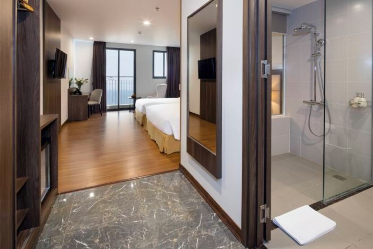 A hotel room with a bed, a desk, a chair, a shower, and a balcony.