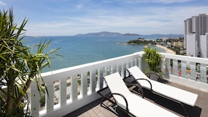 A balcony with white railings, two white lounge chairs, and a view of the sea and distant mountains. - Daphovina Hotel (Bac Nha Trang)