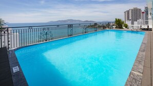 A swimming pool with a view of the ocean and mountains, surrounded by a metal fence and a wooden deck. - Daphovina Hotel (Bac Nha Trang)