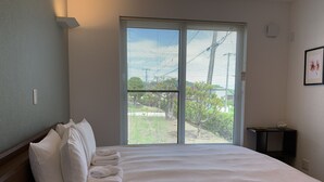 A neatly made bed with pillows and a folded towel, a window with blinds, and a small table with a bowl of fruit. - Diamond Dust Furano (Furano)