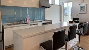 A modern kitchen with white cabinets, a large island with bar stools, and a window providing natural light. - Diamond Dust Furano (Furano)