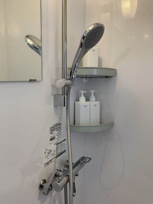 Une salle de bain moderne équipée d’une douche, d’un miroir et d’une étagère où sont rangés les produits de toilette.