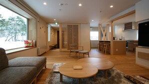 A modern living room with a sofa, two round tables, and a view of the outside. - Asanoha (Furano)