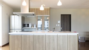 A modern kitchen with a large island, built-in appliances, pendant lighting, and a view into the dining area. - Furano Lookout (Nakafurano)