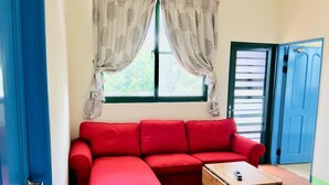 A room with a red sofa, a small wooden table, a window with curtains, and a blue door. - Summer Homestay (Hengchun)
