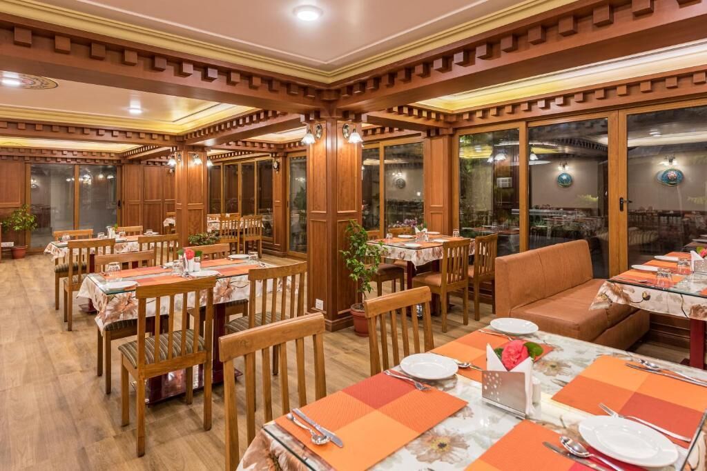 Un restaurante con paneles de madera, mesas dispuestas con manteles individuales anaranjados y amplios ventanales.