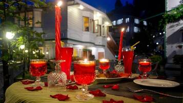 An outdoor dining setup with candles, red drinks, and rose petals on a table.