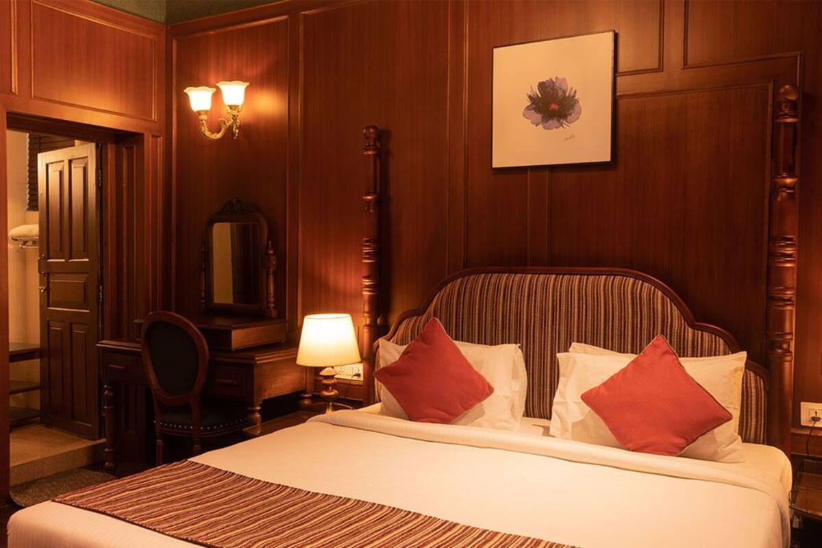 Een hotelkamer met een groot bed, houten lambrisering, een spiegel, een bureau en twee wandlampen.
