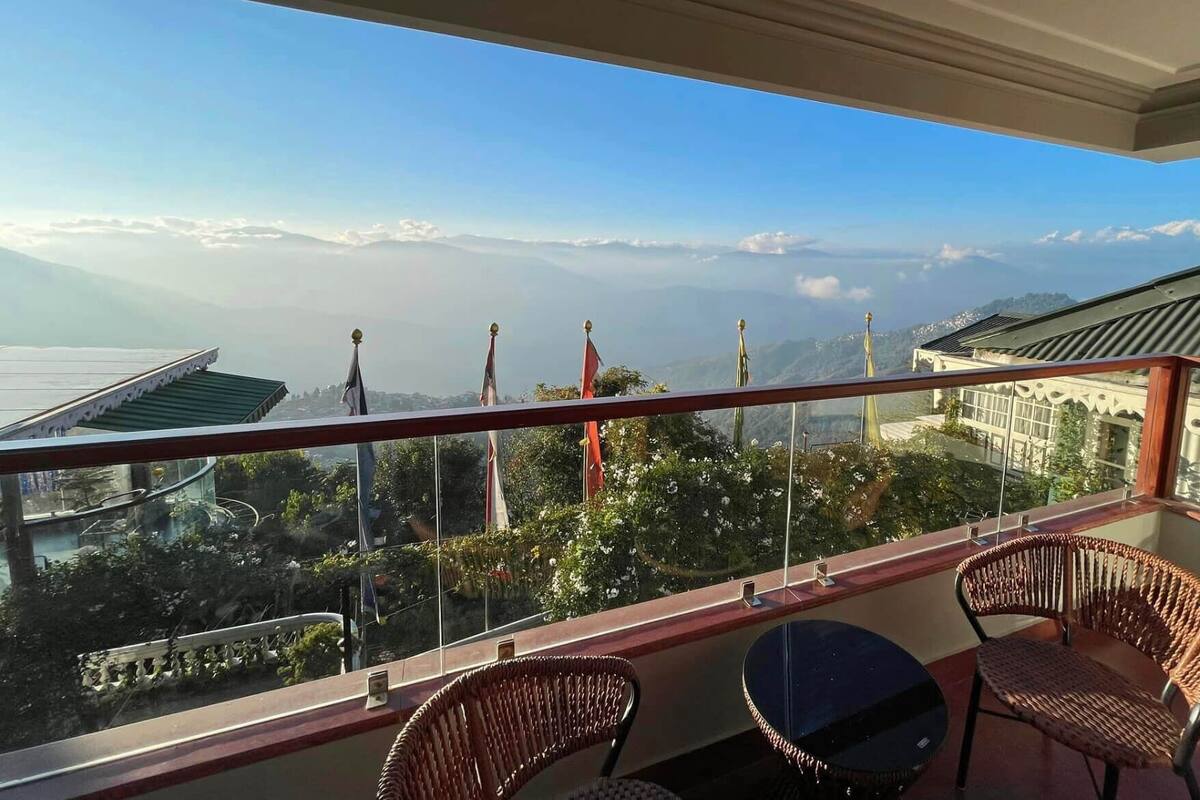 Een balkon met rieten stoelen en een tafel, met uitzicht op een bergachtig landschap met vlaggen.