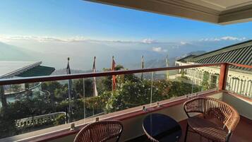 Uma varanda com cadeiras de vime e uma mesa, com vista para uma paisagem montanhosa com bandeiras.