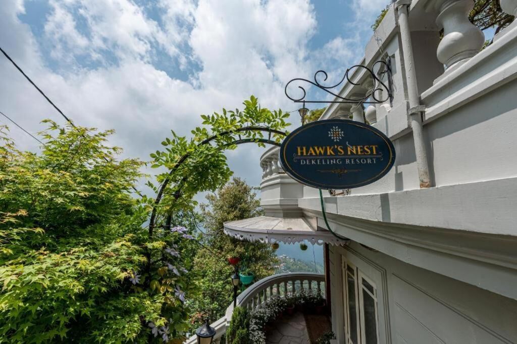Segnaletica dell'hotel 'Hawk's Nest', con vista su vegetazione rigogliosa e un edificio bianco.