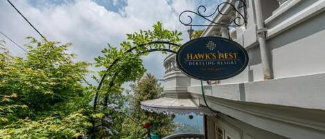 Segnaletica dell'hotel 'Hawk's Nest', con vista su vegetazione rigogliosa e un edificio bianco.