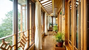 A wooden balcony with large windows, curtains, and potted plants. - Udaan Dekeling Resort Darjeeling (Darjeeling)