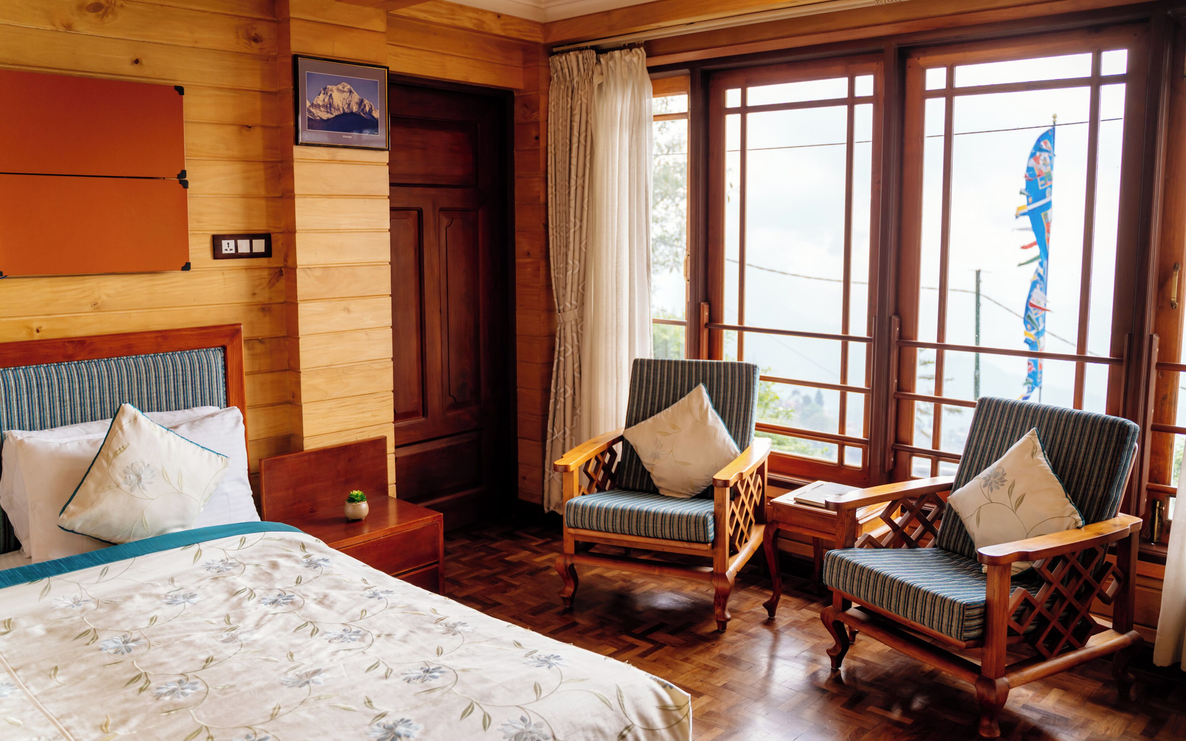 A wooden room with a bed, two armchairs, a wooden nightstand, and a window with curtains.