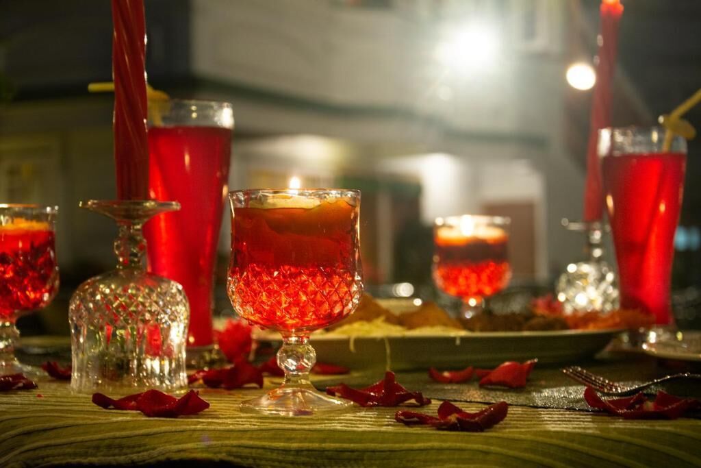 A table with red drinks, a candle, and scattered rose petals.