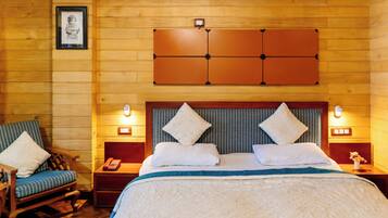 A wooden-paneled room with a bed, two bedside tables, a chair, and a framed picture on the wall.