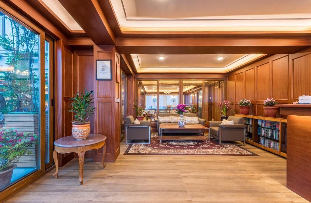 A spacious lobby with wooden paneling, a seating area with sofas and a coffee table, a small side table with a plant, and a bookshelf filled with books.