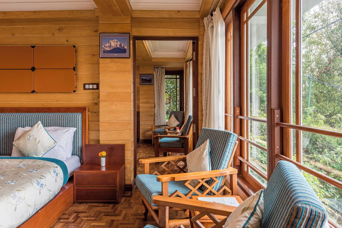 Houten cabinestijl interieur met een bed, twee stoelen, een kleintje tafel en een raam met uitzicht op bomen.