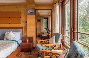 Houten cabinestijl interieur met een bed, twee stoelen, een kleintje tafel en een raam met uitzicht op bomen.