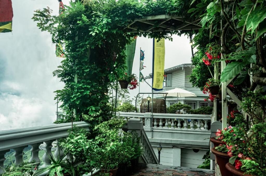 A covered outdoor area with a railing, potted plants, and a building in the background.