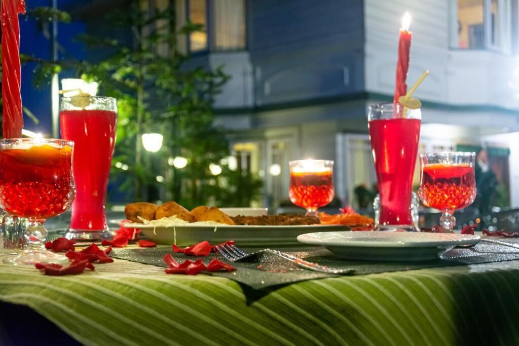 A table set for a meal with red drinks, a candle, and scattered rose petals.