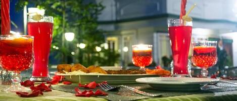Une table mise pour un repas, avec des boissons rouges, une bougie et des pétales de rose éparpillés.