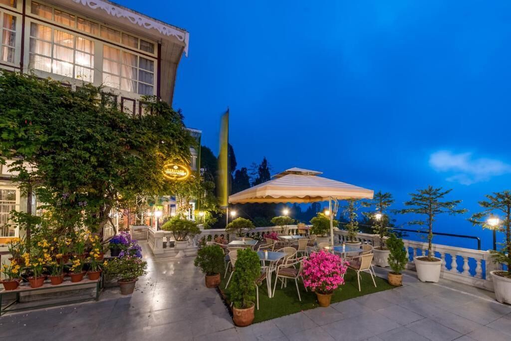 Una terraza al aire libre con mesas y sillas, plantas en macetas y un edificio con balcón.