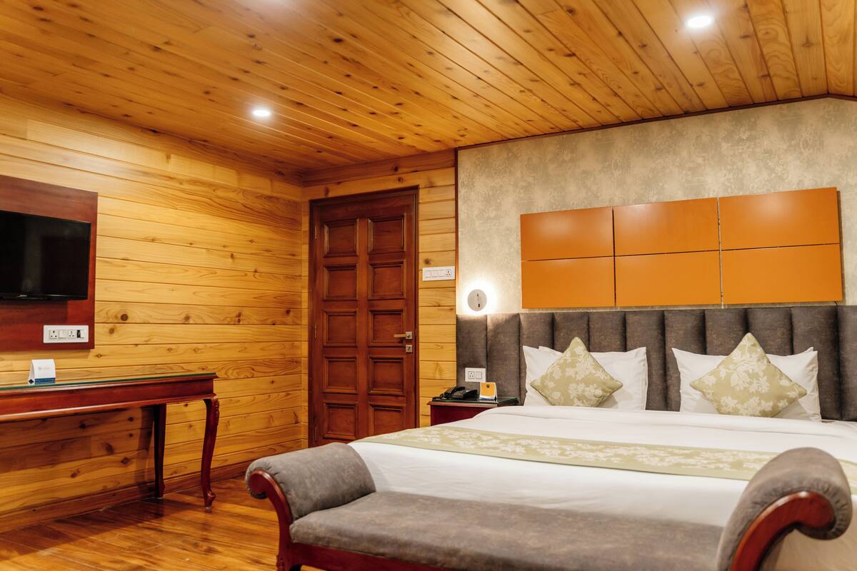 Een kamer met houten lambrisering, een bed, een bureau, een televisie en een nachtkastje.