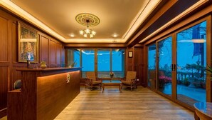 A reception area with a wooden reception desk, two armchairs, a chandelier, and large windows offering a view of the outdoors. - Udaan Dekeling Resort Darjeeling (Darjeeling)