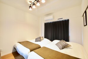 A hotel room with two beds, a ceiling light fixture, an air conditioning unit, and a window with curtains.