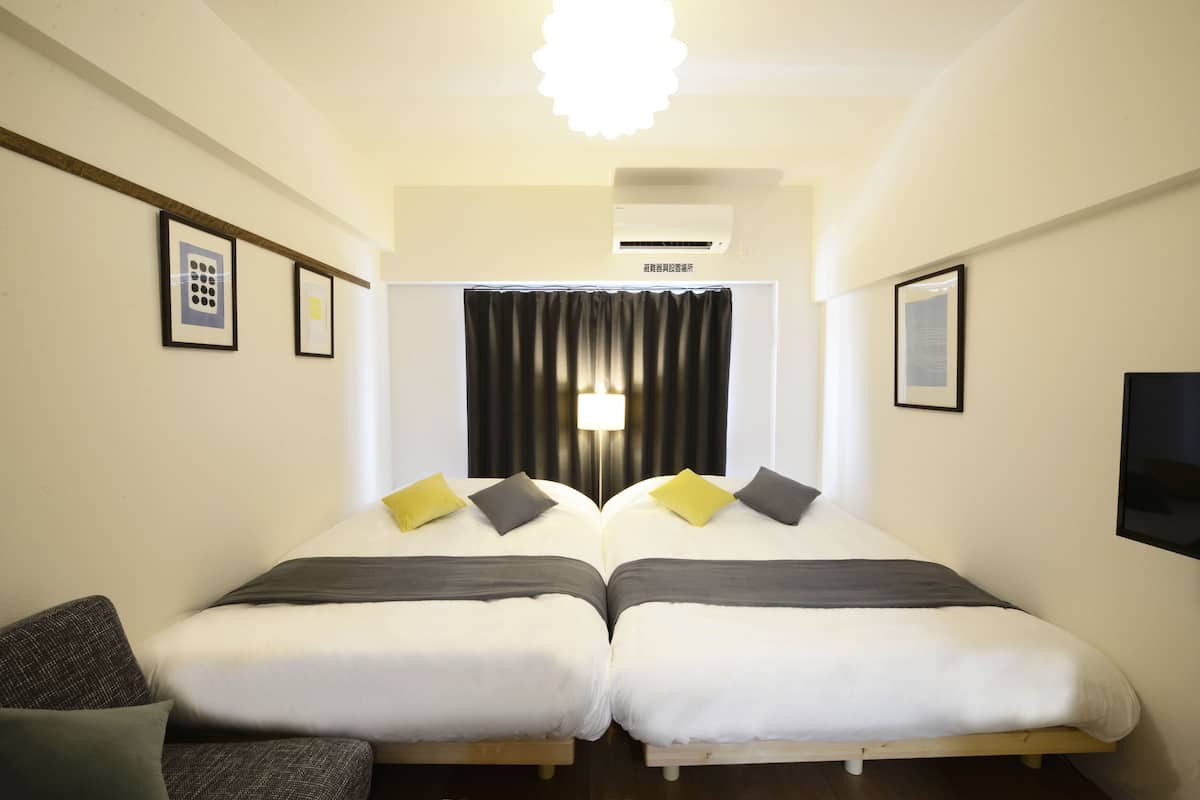 A hotel room with two single beds, a sofa, a ceiling light, and framed pictures on the walls.